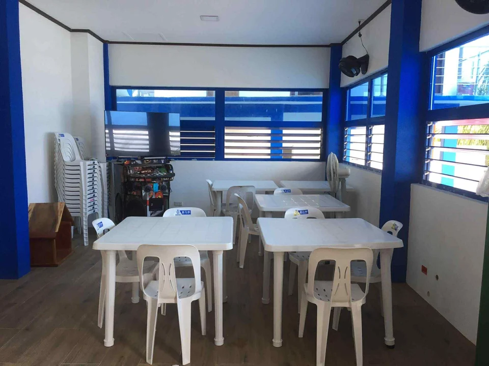 Indoor gathering area with white tables and chairs and a videoke setup